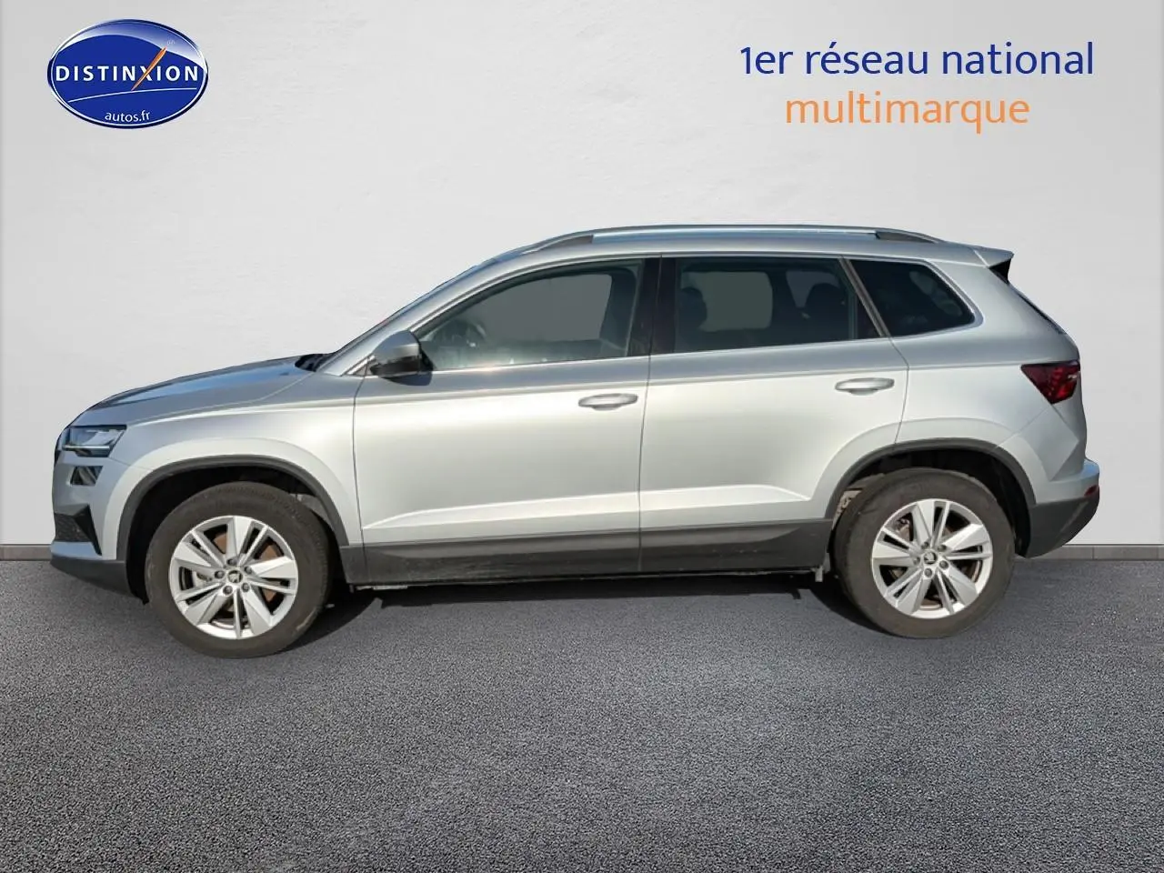 Vue de profil côté gauche d'un Skoda Karoq gris 2025 avec jantes alliage et barres de toit.