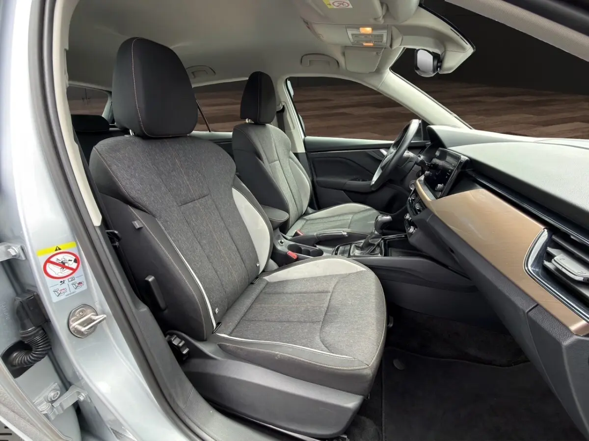 Vue intérieure côté conducteur du Skoda Kamiq 2023 gris clair, montrant sièges tissu bicolore et tableau de bord bois clair.