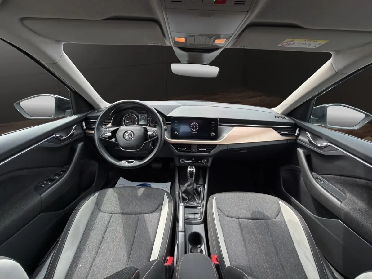 Vue avant intérieure du Skoda Kamiq 2023 avec tableau de bord clair, volant cuir multifonctions et sièges bi-ton gris.