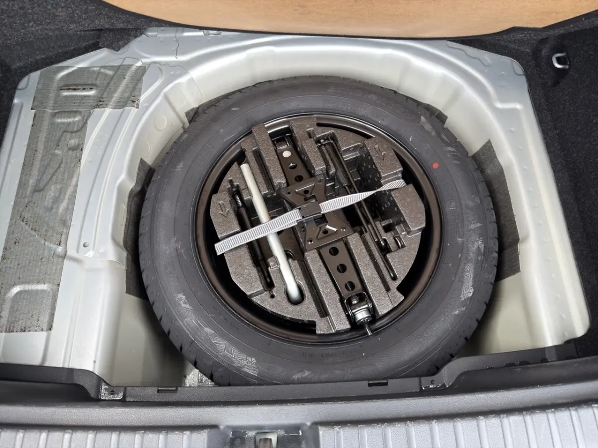 Gros plan sur la roue de secours galette noire et ses outils, logée dans le coffre du Skoda Kamiq gris clair 2023.