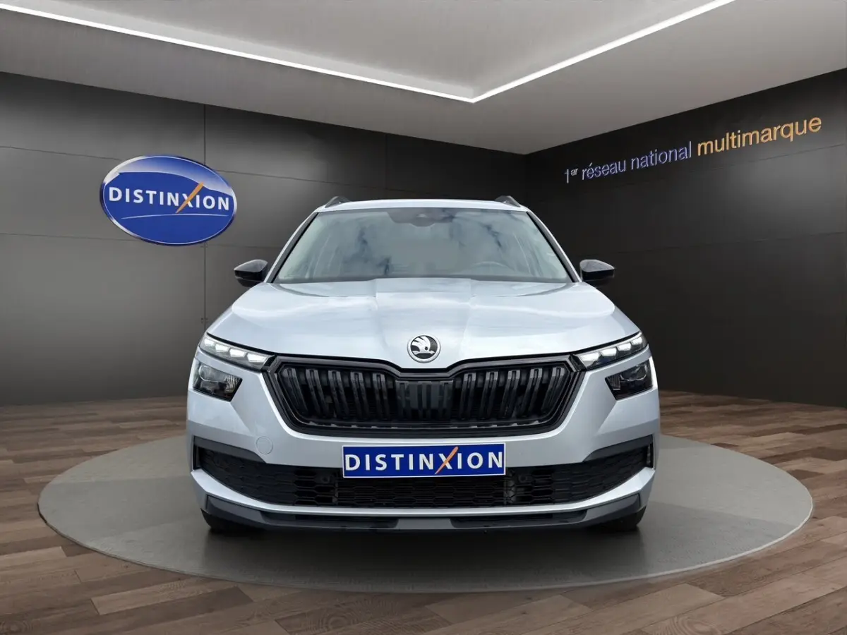 Vue avant d'un Skoda Kamiq gris clair avec calandre noire et feux LED, présenté en showroom Distinxion.