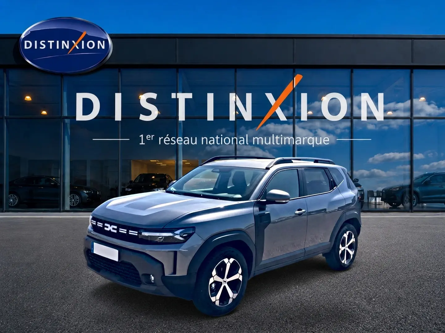 Vue 3/4 avant droit du Dacia Duster gris schiste avec jantes alu et barres de toit devant une vitrine Distinxion.
