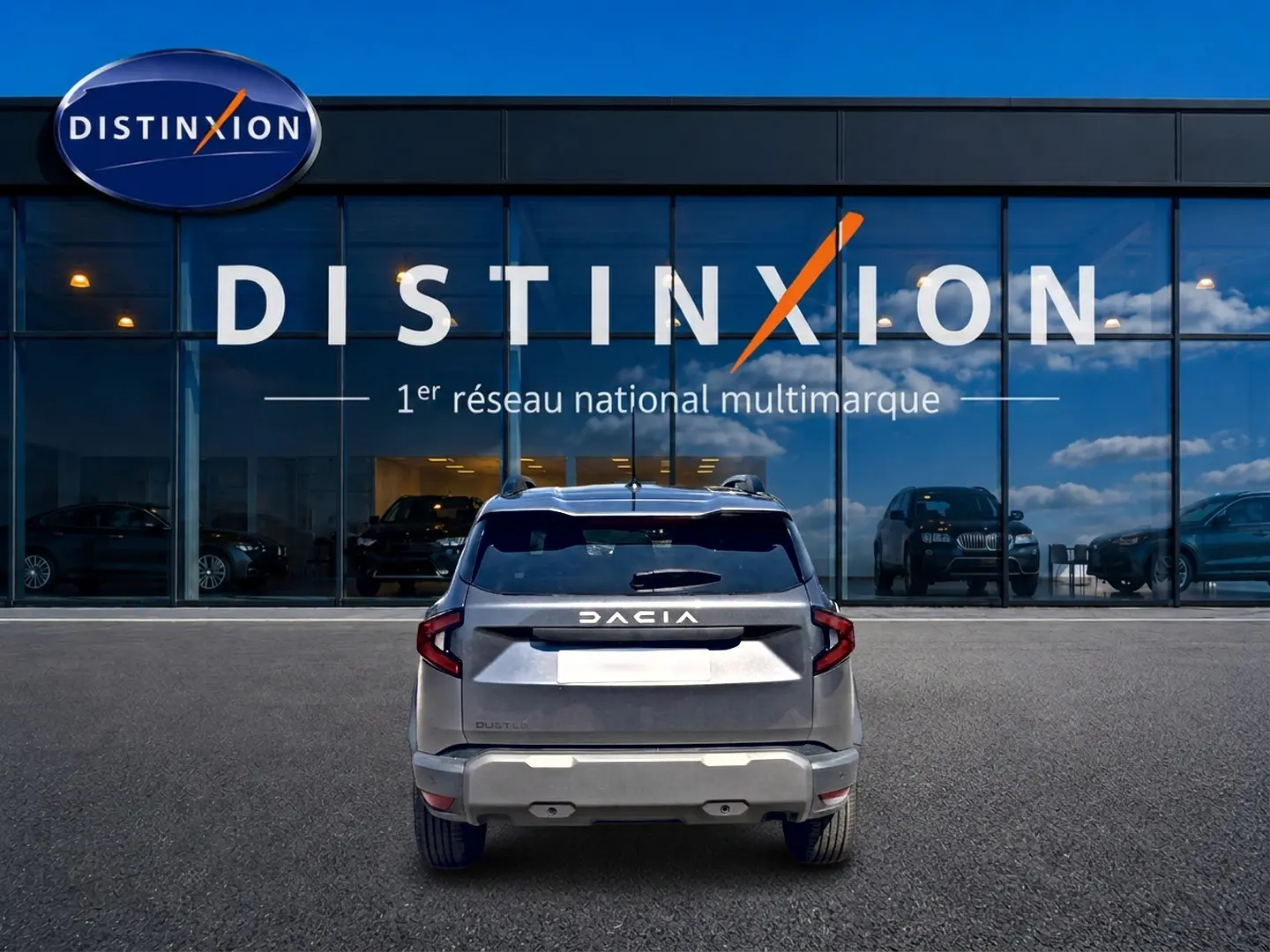 Vue arrière d'un Dacia Duster gris schiste 2026 garé devant une vitrine avec logo Distinxion.