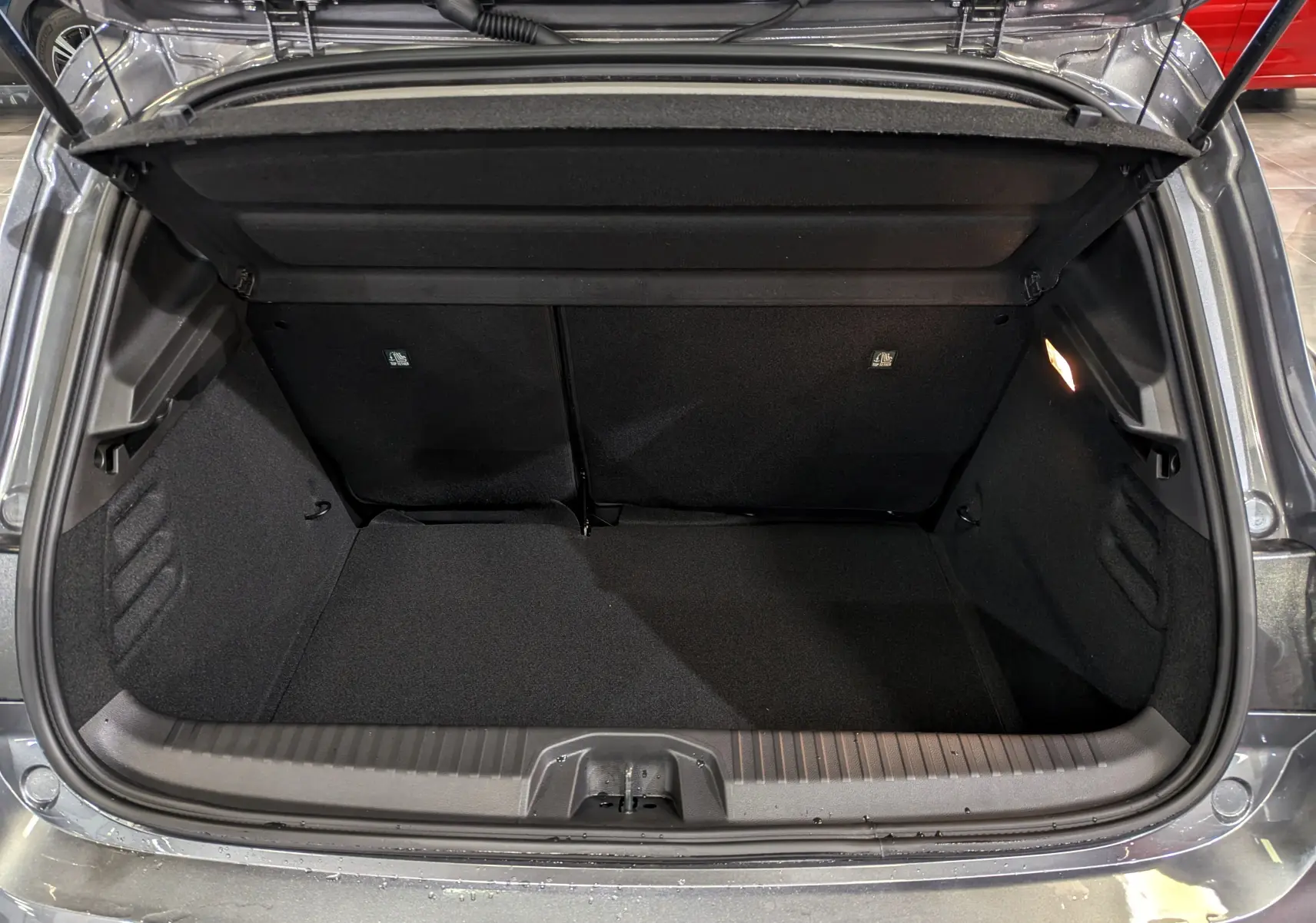 Coffre ouvert vu de l'arrière d'une Renault Clio V Blue dCi 100 CH Evolution gris schiste, intérieur noir et éclairage latéral.