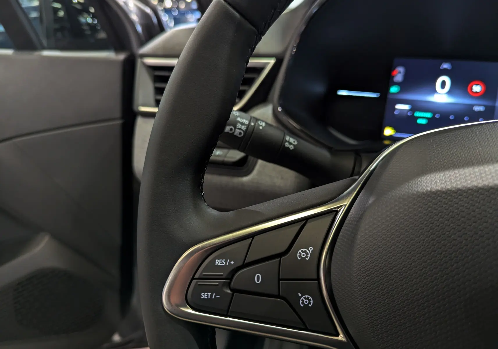 Gros plan sur le volant noir de la Renault Clio V 2025 avec commandes de régulateur de vitesse et tableau de bord numérique.