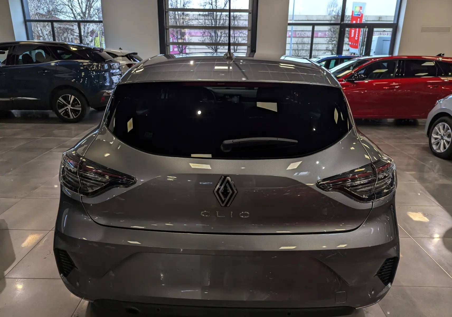 Vue arrière d'une Renault Clio V gris schiste 2025 en showroom, avec feux arrière LED et vitre teintée.