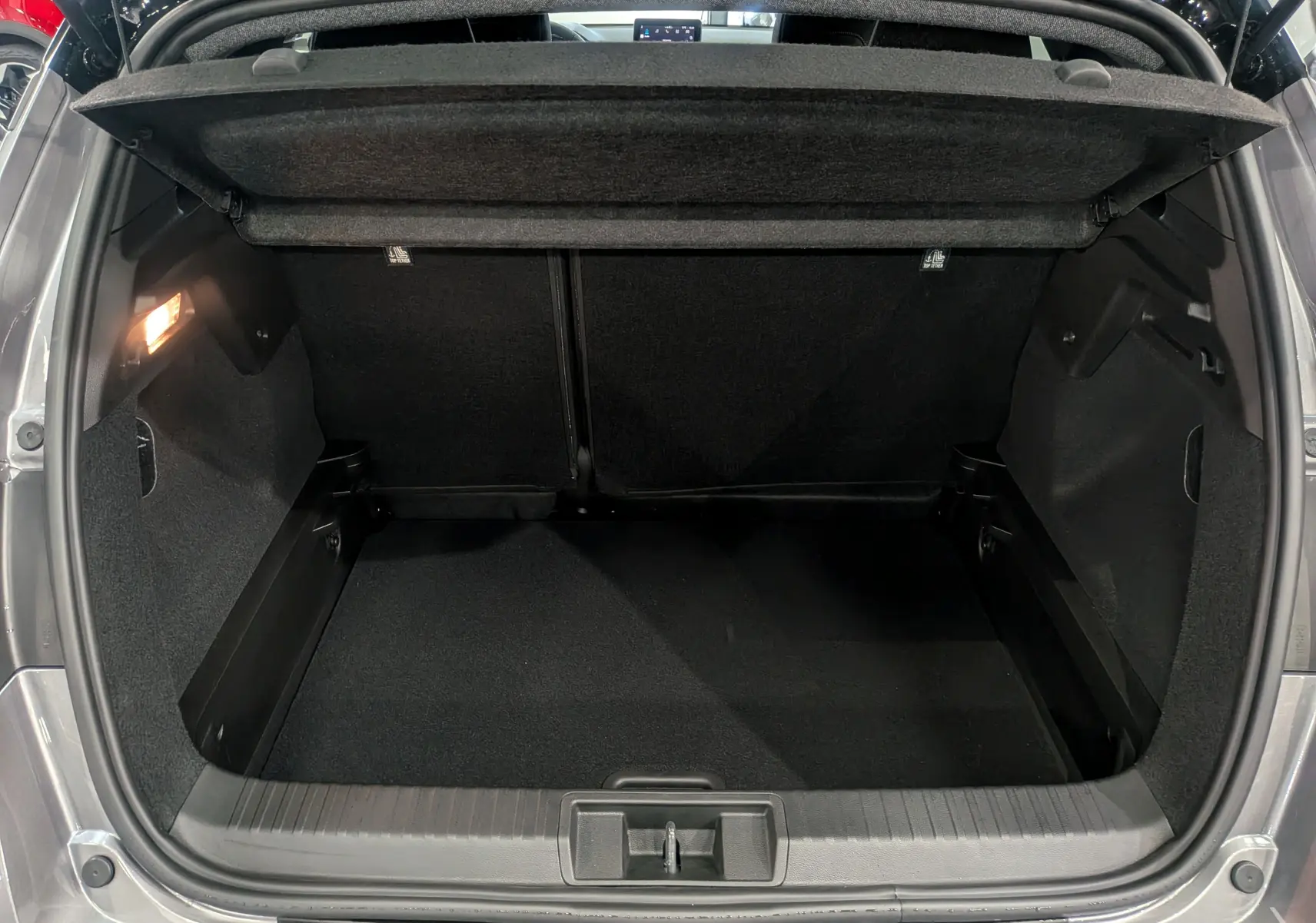 Coffre ouvert vu de l'arrière d'un Renault Captur 2025 gris Cassiopé avec intérieur noir et éclairage latéral.