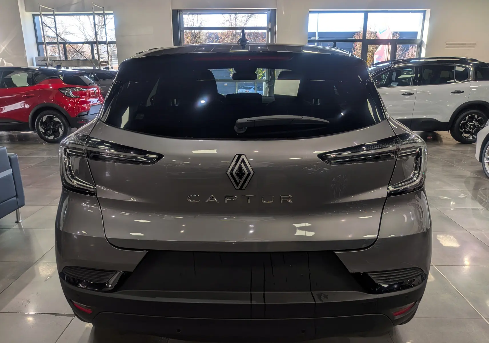 Vue arrière d'un Renault Captur 2025 gris Cassiopé avec toit noir, en intérieur de showroom lumineux.