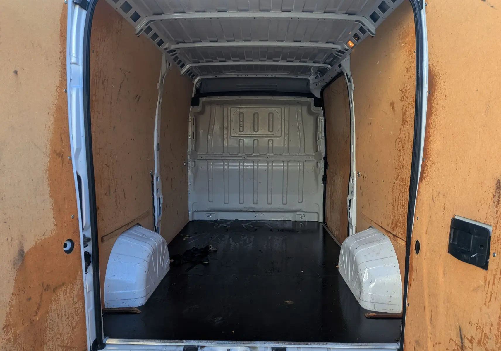 Vue intérieure arrière du fourgon blanc Fiat Ducato 2022, montrant l’espace de chargement avec parois en bois et sol noir.