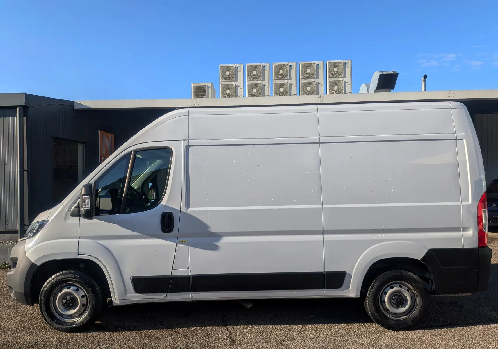 Vue de profil côté gauche d'un fourgon FIAT Ducato blanc 2022 avec carrosserie haute et longue, roues acier et bandeau noir.