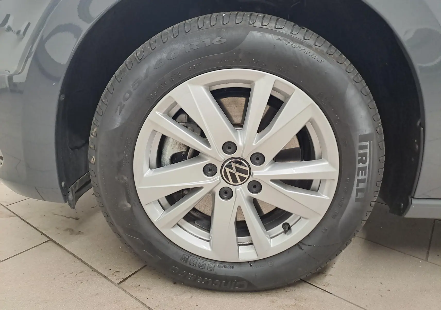 Gros plan sur la roue avant droite du Volkswagen Touran gris Dauphin avec jante alliage et pneu Pirelli.