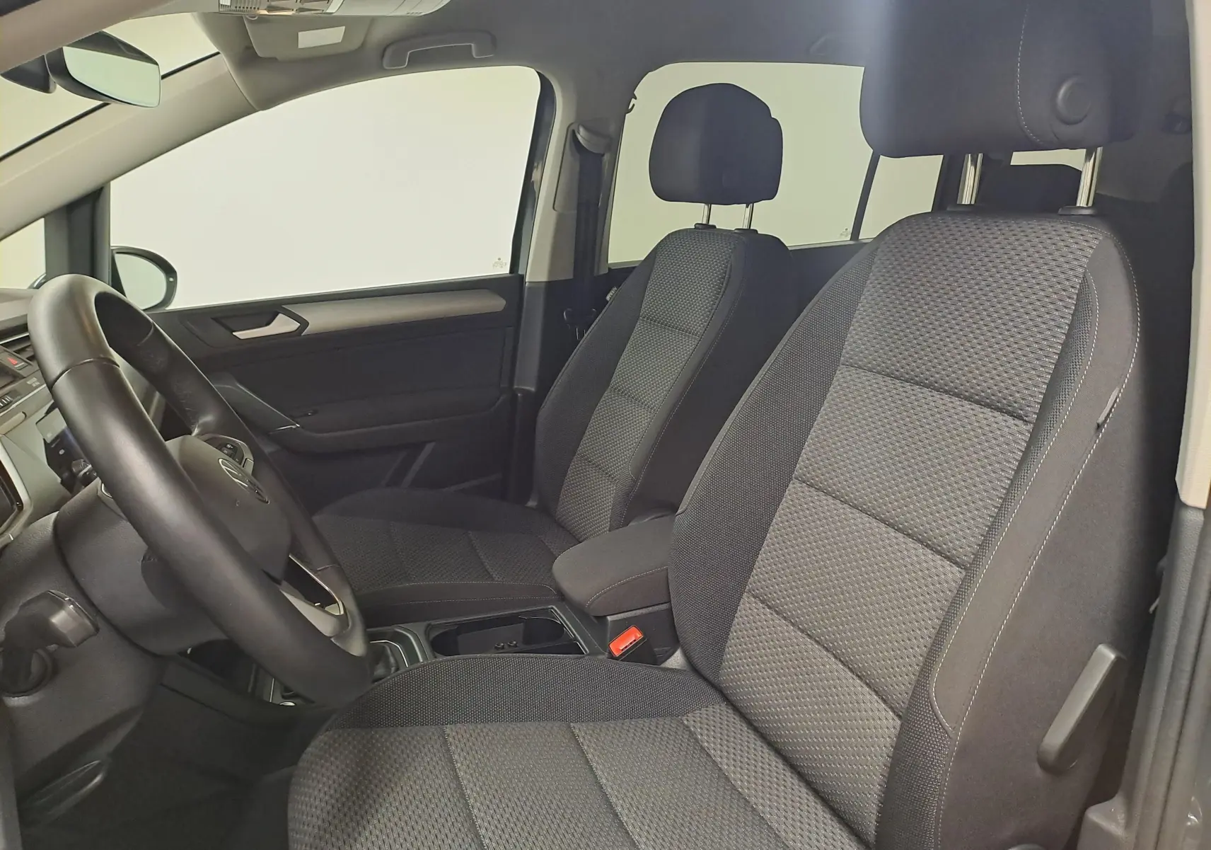 Vue intérieure côté conducteur du Volkswagen Touran 2024, sièges tissu gris et volant multifonction noir.