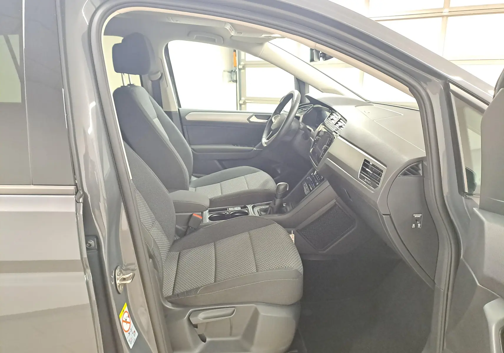 Vue intérieure côté conducteur du Volkswagen Touran gris Dauphin 2024, montrant les sièges avant et le tableau de bord.