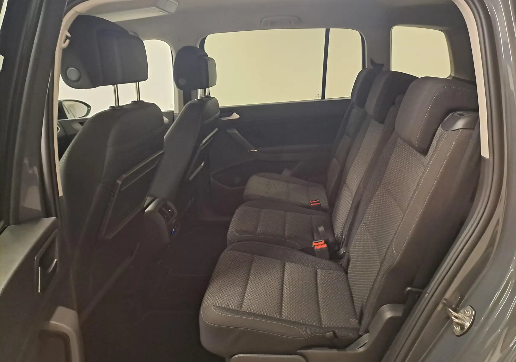 Vue intérieure côté droit du Volkswagen Touran 2024 gris Dauphin, montrant les sièges arrière en tissu noir et les appuie-têtes.