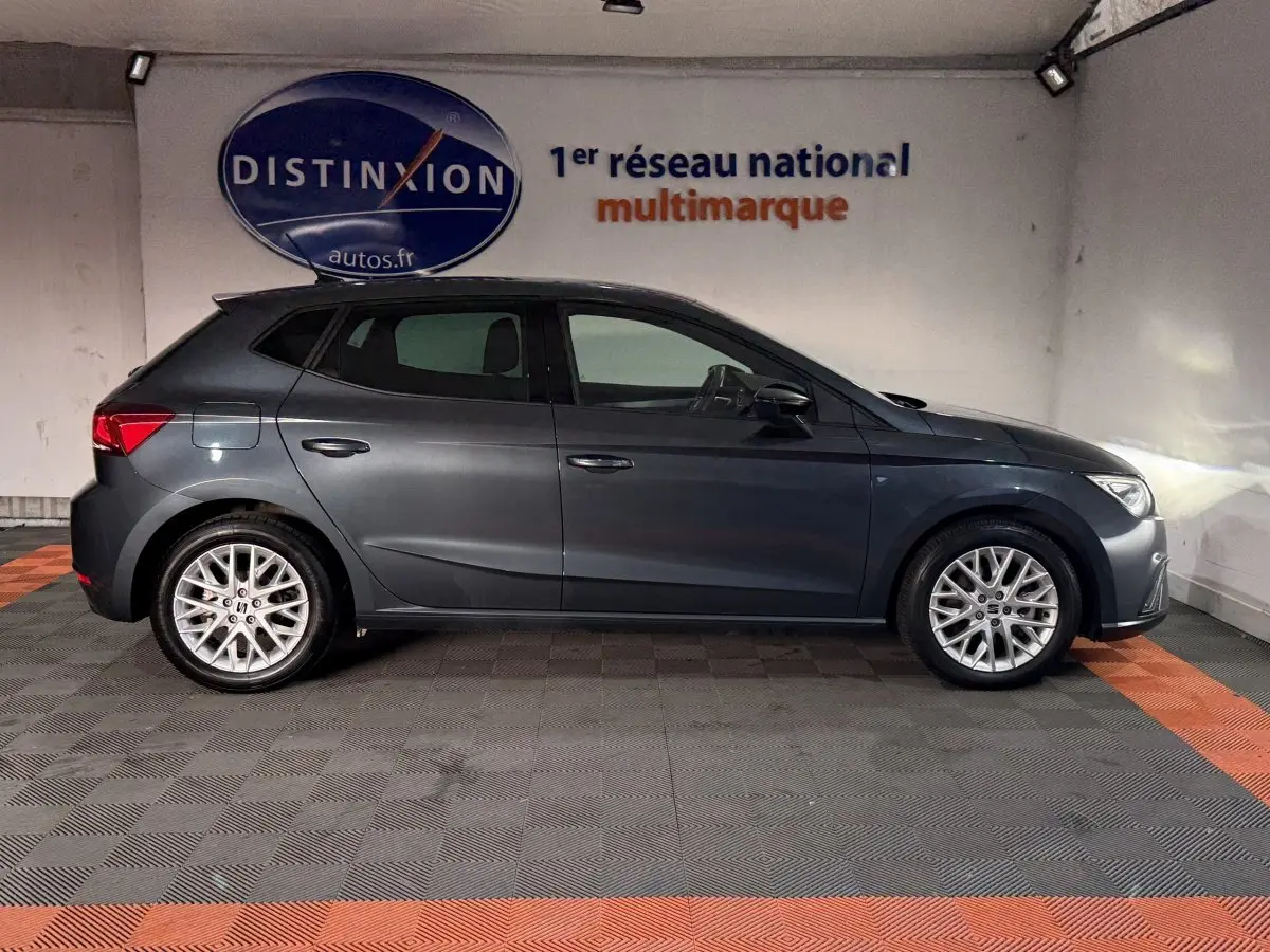 Vue de profil côté gauche d'une SEAT Ibiza 1.0 TSI 110 FR gris foncé, avec jantes alliage et phares allumés.
