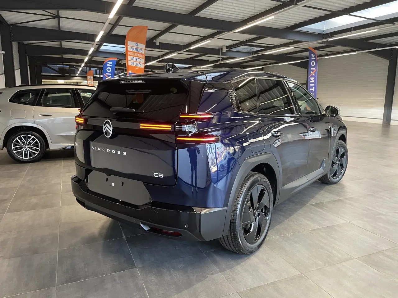 Vue 3/4 arrière droite du Citroën C5 Aircross bleu Azul avec feux arrière LED allumés en showroom.