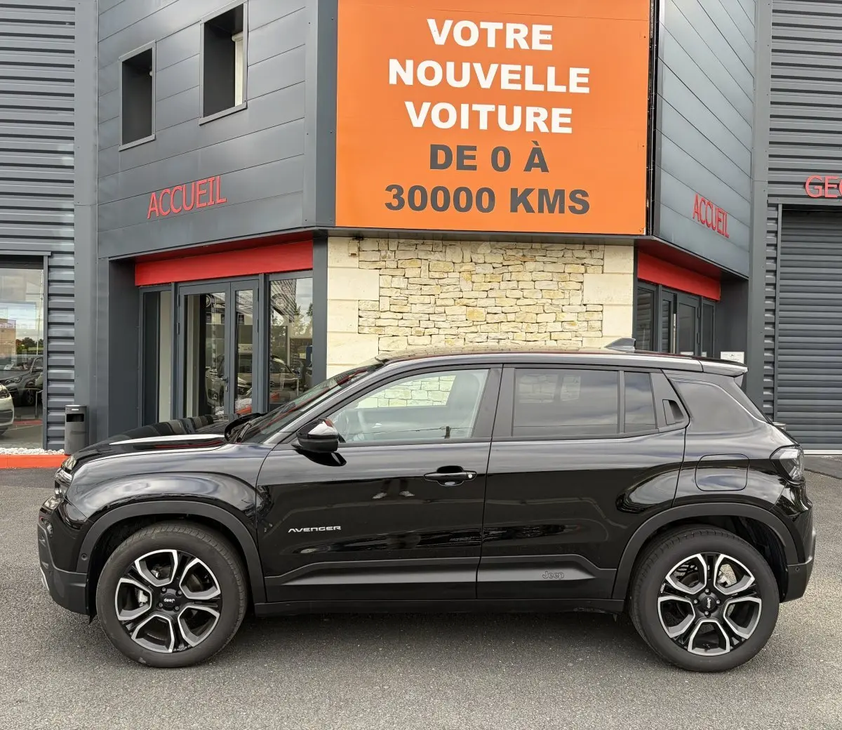 Vue de profil côté gauche d'un Jeep Avenger noir 2025 garé devant un bâtiment avec panneau orange.
