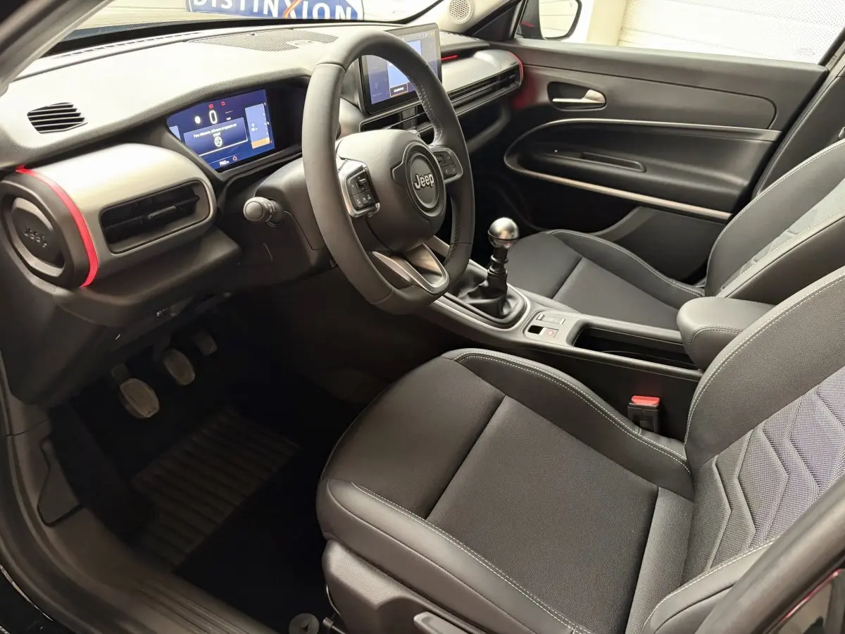 Intérieur Jeep Avenger 2025 vu côté conducteur, tableau de bord noir avec touches rouges et volant cuir multifonctions.