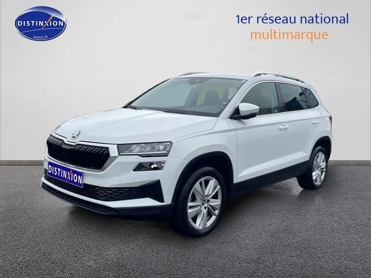 Vue 3/4 avant droite d’un Skoda Karoq blanc glacial avec jantes alu et barres de toit visibles.