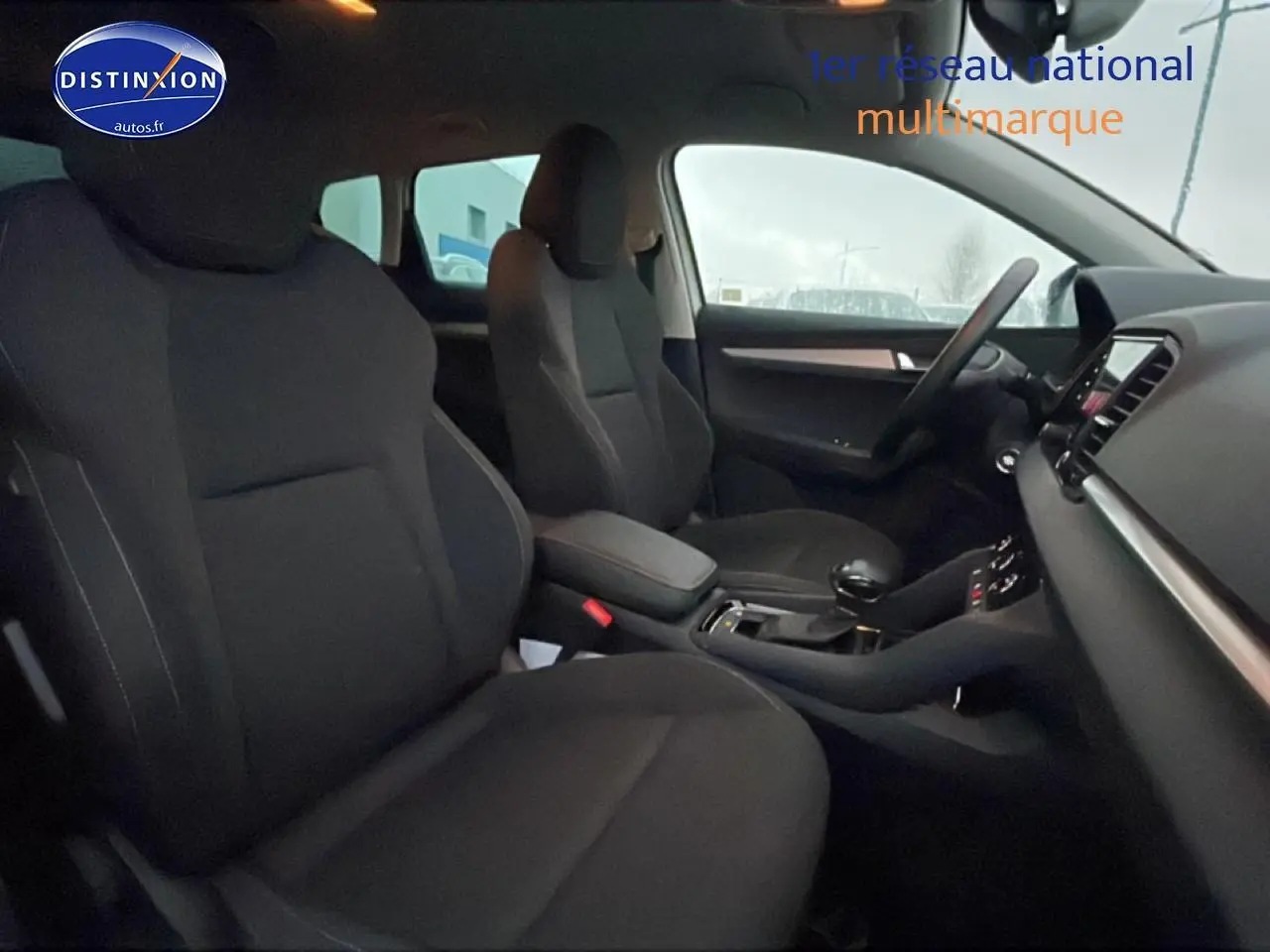 Vue intérieure côté avant droit du Skoda Karoq blanc glacial, montrant sièges noirs et console centrale avec boîte auto.