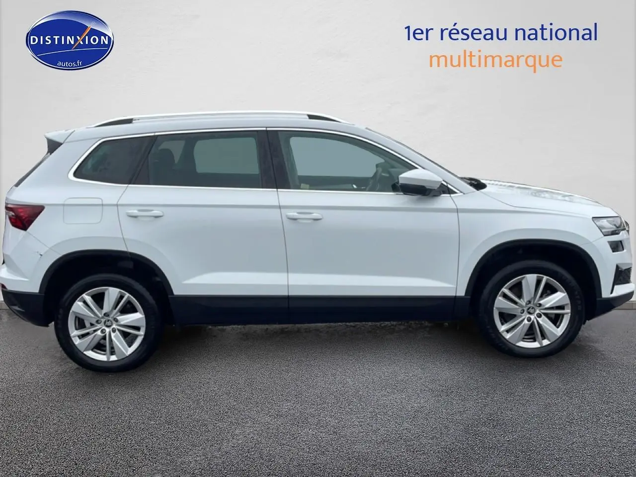 Vue latérale droite d'un Skoda Karoq blanc glacial avec jantes alu et barres de toit visibles.