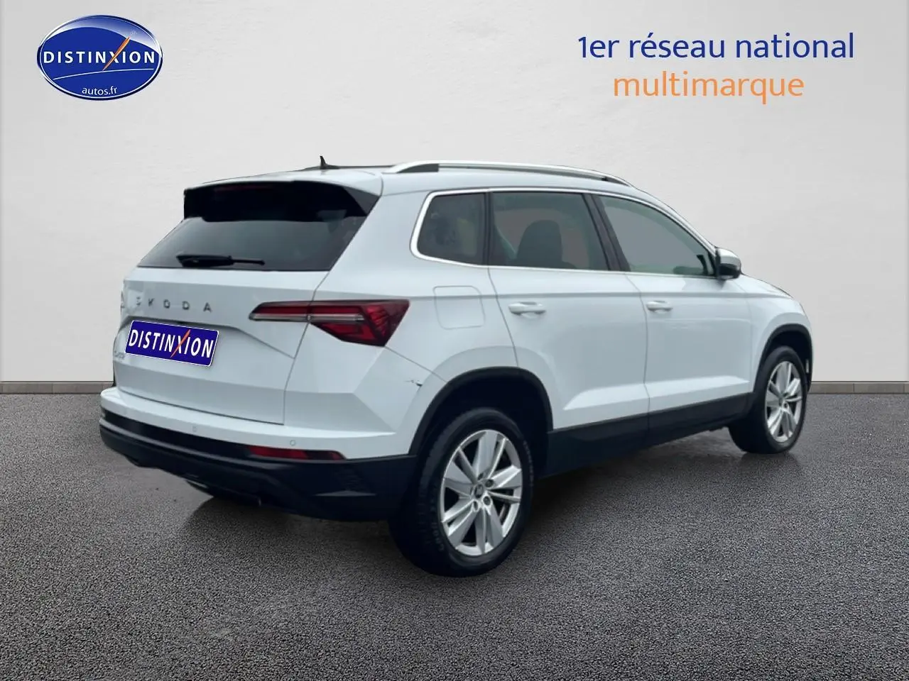 Vue 3/4 arrière droite d'un Skoda Karoq blanc glacial avec jantes alu et barres de toit visibles.