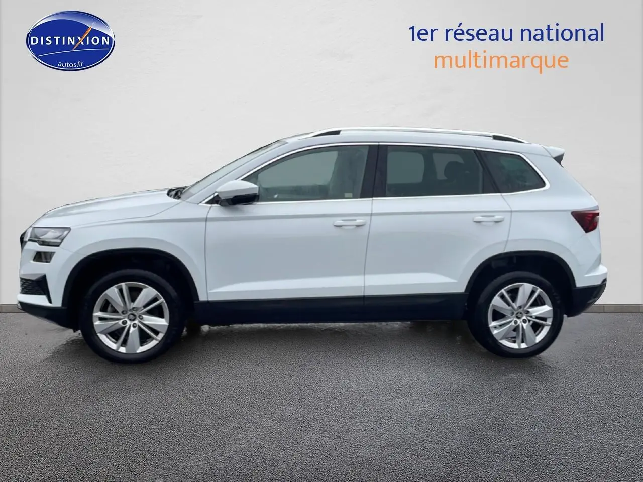 Vue de profil côté gauche d’un Skoda Karoq blanc glacial avec jantes alliage et barres de toit noires.