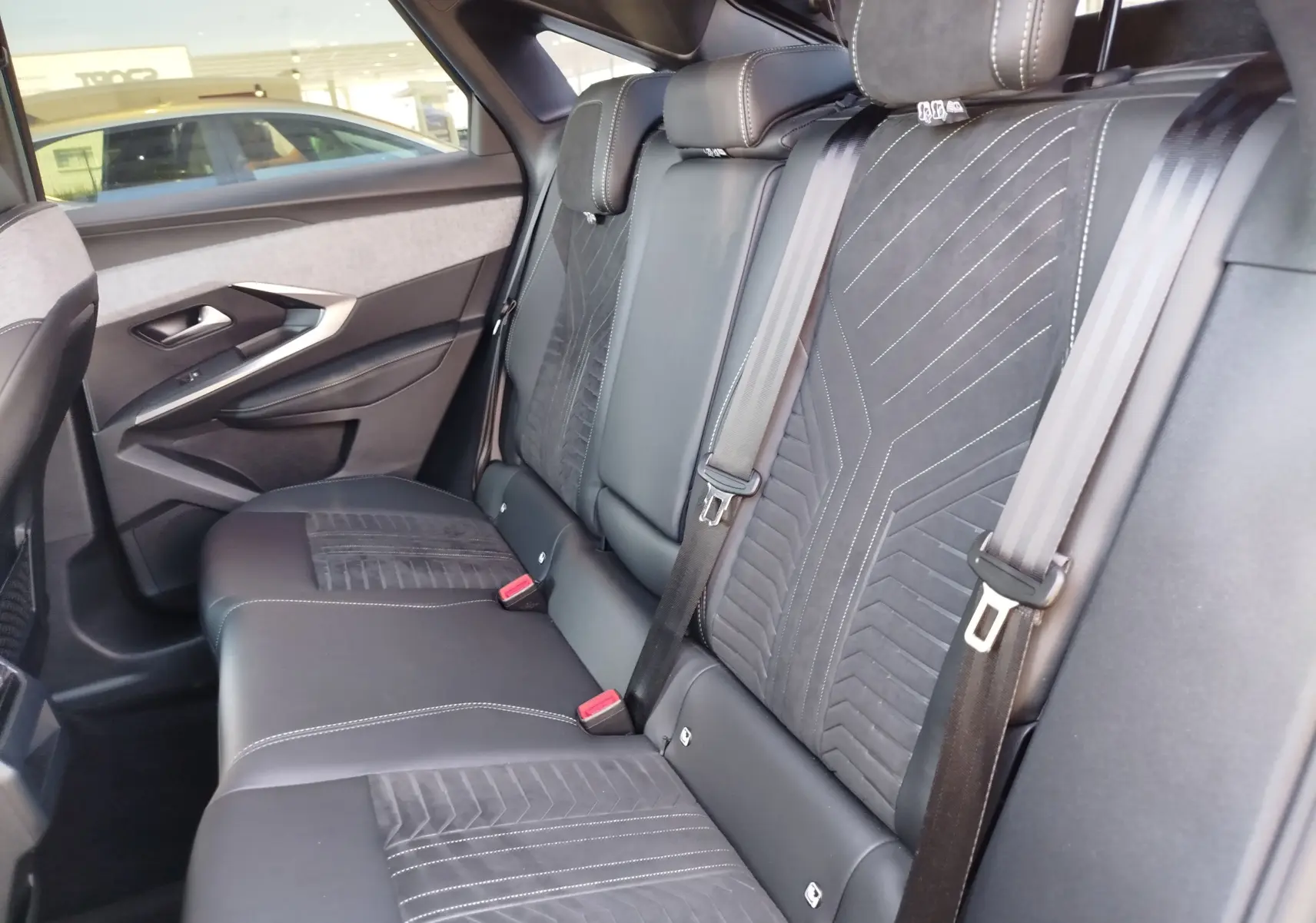 Vue intérieure arrière côté gauche du Peugeot 3008 2024, sièges en cuir noir avec surpiqûres blanches et détails en tissu.