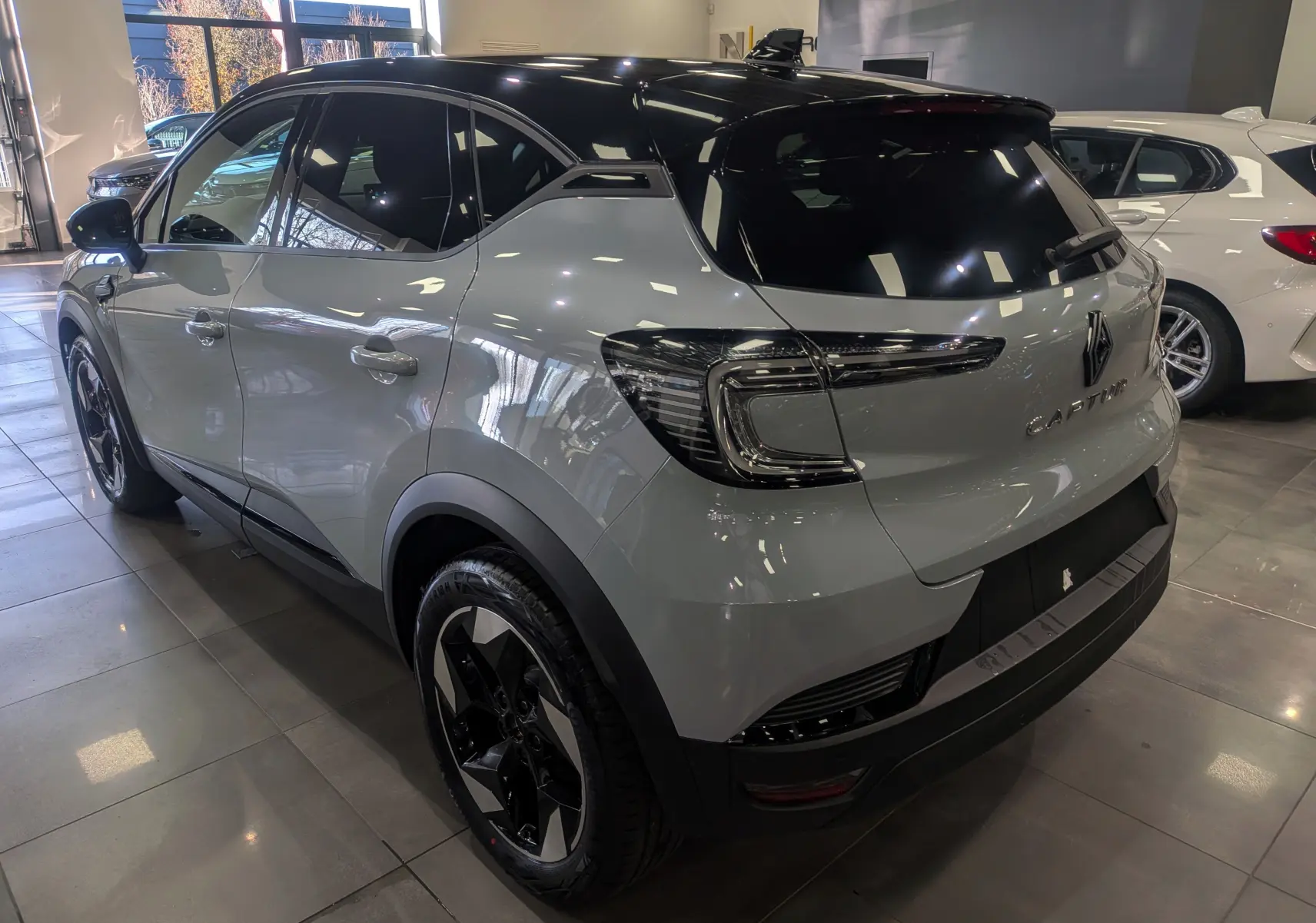 Vue 3/4 arrière gauche du Renault Captur 2025 gris Rafale avec toit noir et feux arrière LED distinctifs.