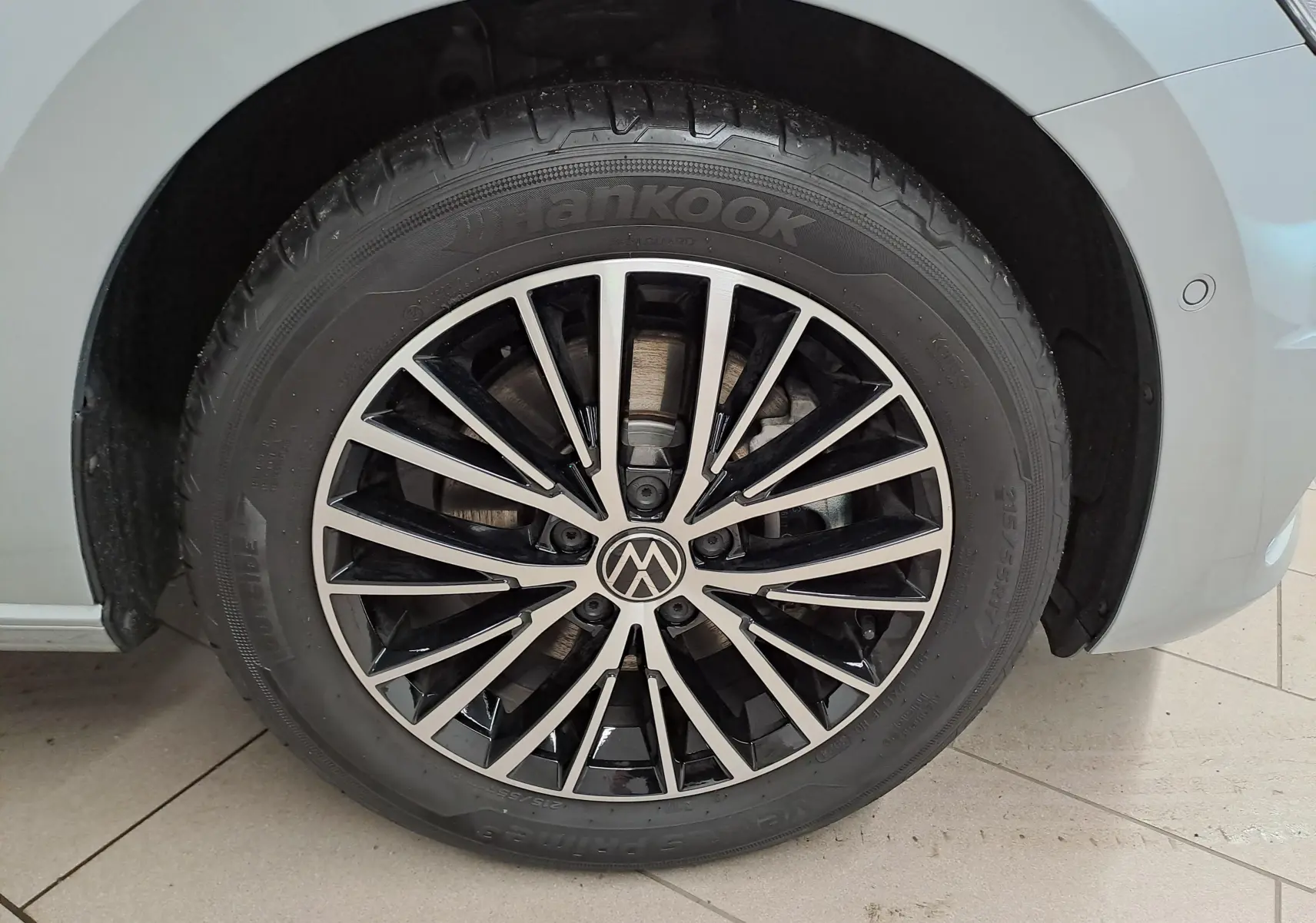 Gros plan sur la roue avant droite du Volkswagen Touran gris argent, mettant en valeur la jante alliage bicolore au design moderne.