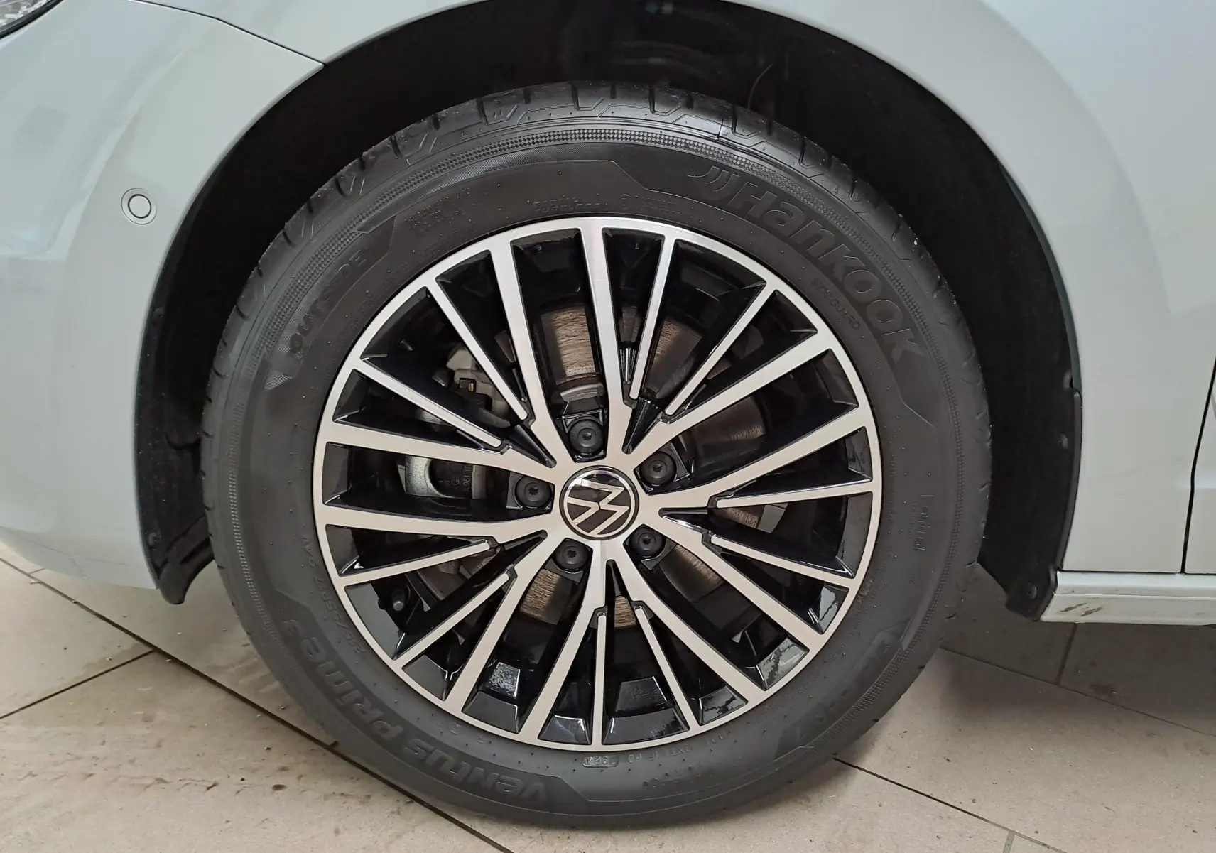 Gros plan sur la roue avant droite d'un Volkswagen Touran gris argent, jante alliage noire et argentée au design moderne.