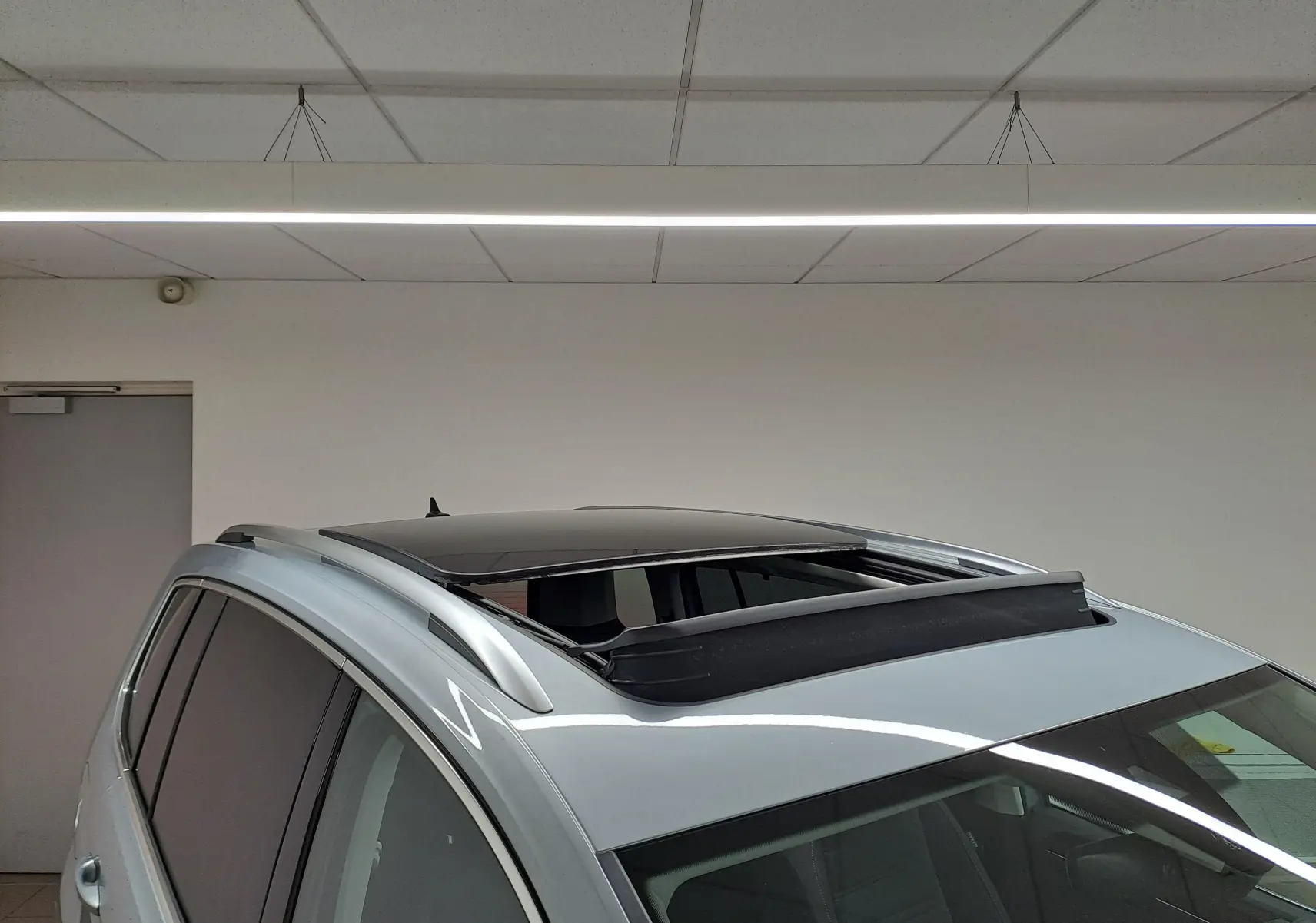 Vue en plongée du toit ouvrant panoramique ouvert d'un Volkswagen Touran gris argent, avec barres de toit visibles.