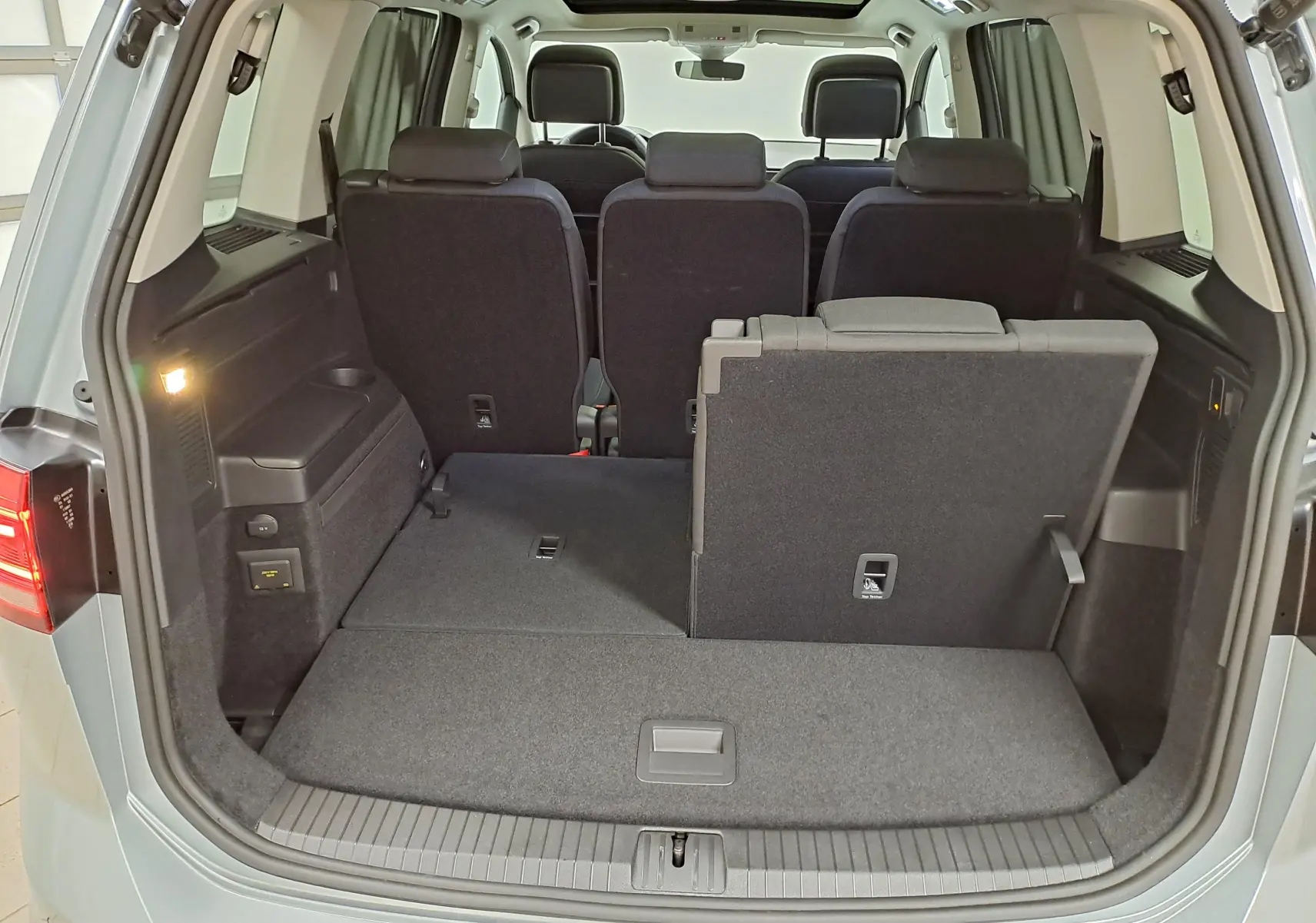 Vue arrière du coffre ouvert du Volkswagen Touran gris argent 2025, montrant la banquette arrière partiellement rabattue.
