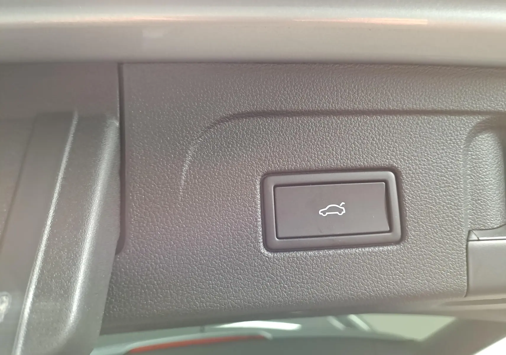 Gros plan sur le bouton d'ouverture électrique du hayon dans le coffre du Volkswagen Touran gris argent 2025.