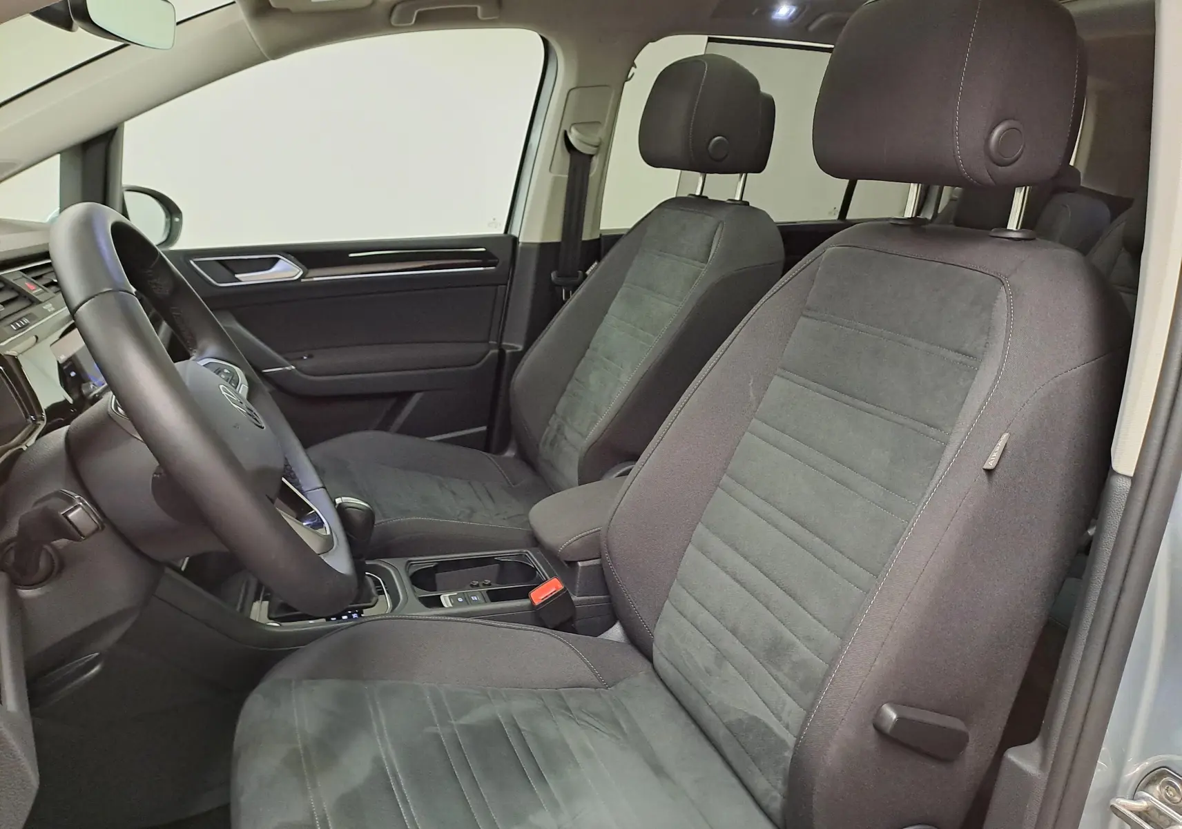 Vue intérieure côté conducteur du Volkswagen Touran 2025, sièges tissu noir avec console centrale et volant visible.