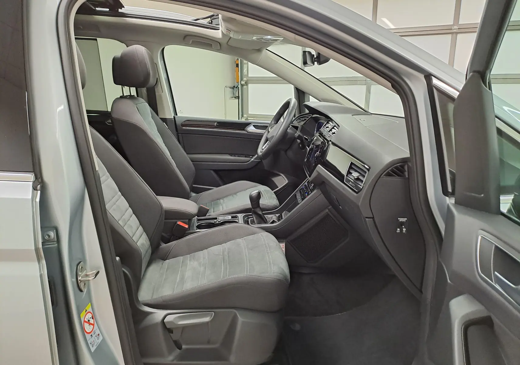 Vue intérieure côté conducteur du Volkswagen Touran gris argent 2025, montrant sièges avant et tableau de bord moderne.