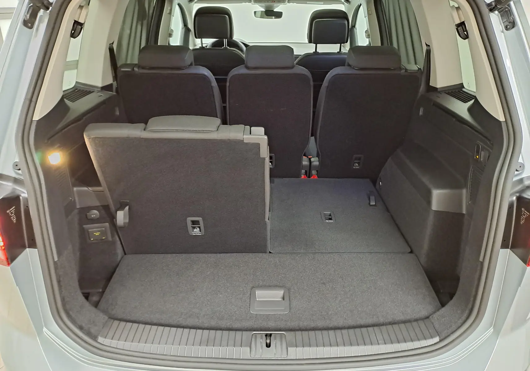 Volkswagen Touran gris argent vu de face, avec phares allumés et toit ouvrant partiellement ouvert.