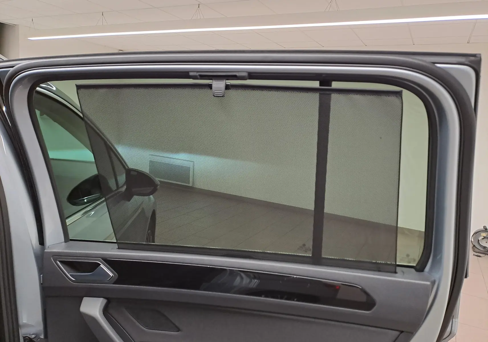 Vue intérieure sur la porte arrière gauche grise argentée d’un Volkswagen Touran 2025 avec store pare-soleil déployé.