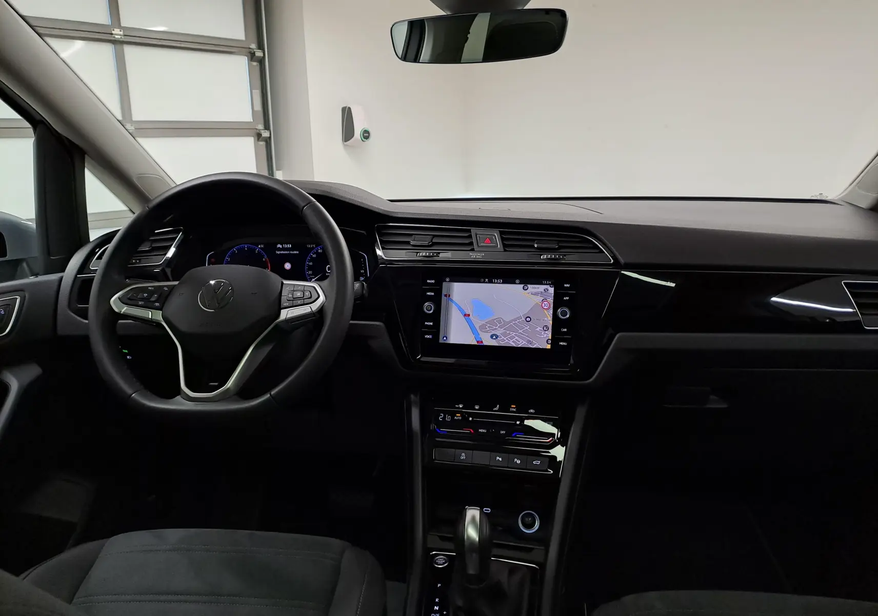 Vue intérieure avant du Volkswagen Touran 2025 avec tableau de bord noir et écran tactile affichant une carte de navigation.