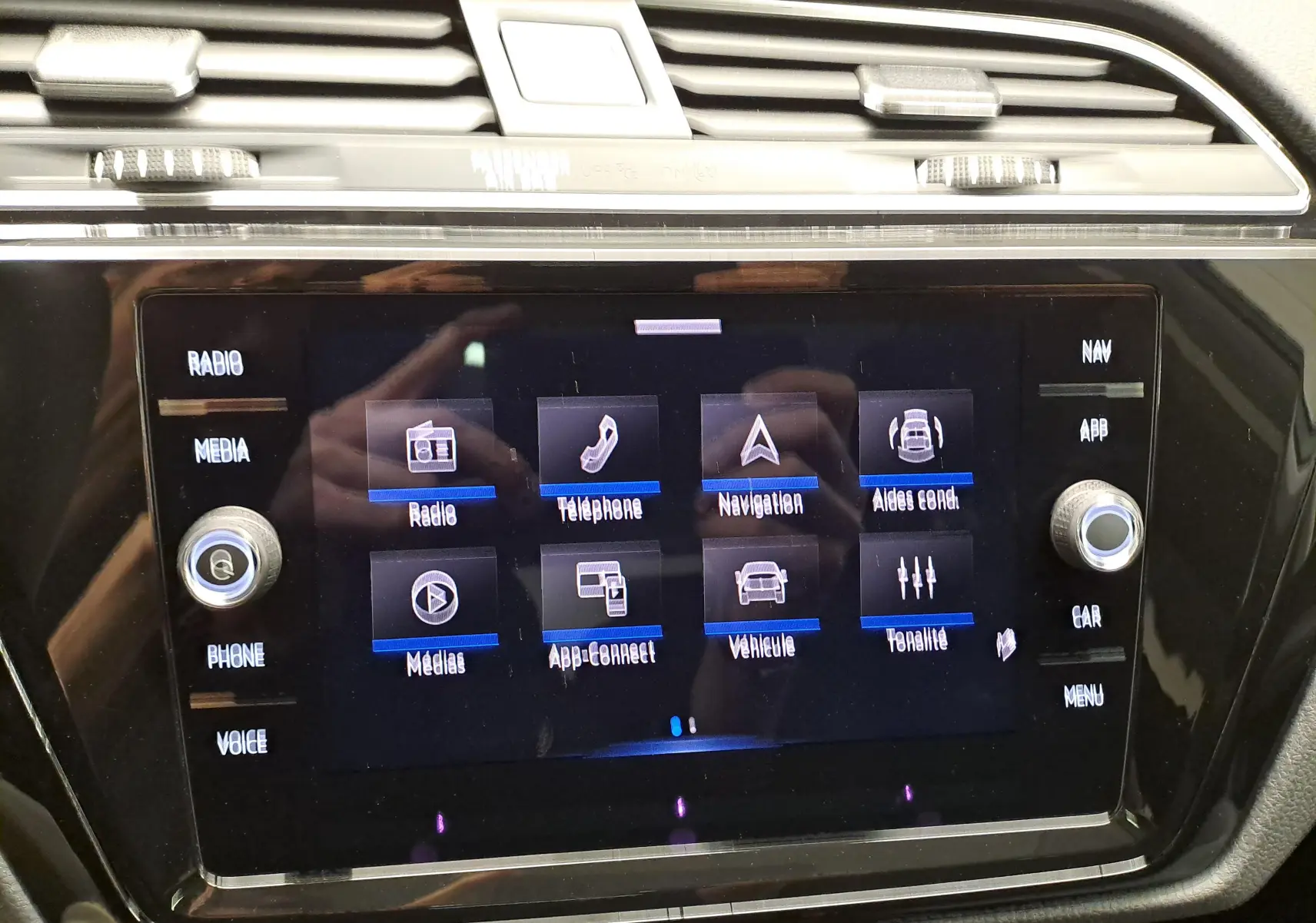 Écran tactile central du tableau de bord du Volkswagen Touran 2025 affichant les menus radio, téléphone, navigation et aides à la conduite.