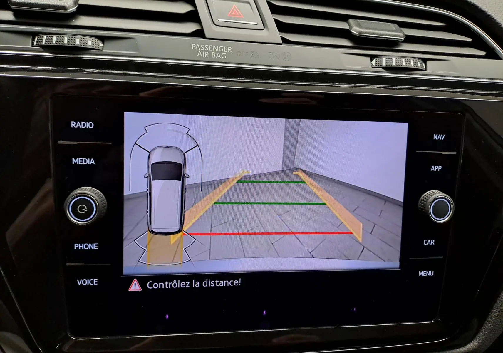 Écran de caméra de recul du Volkswagen Touran gris argent montrant les lignes de guidage et l'alerte de distance.