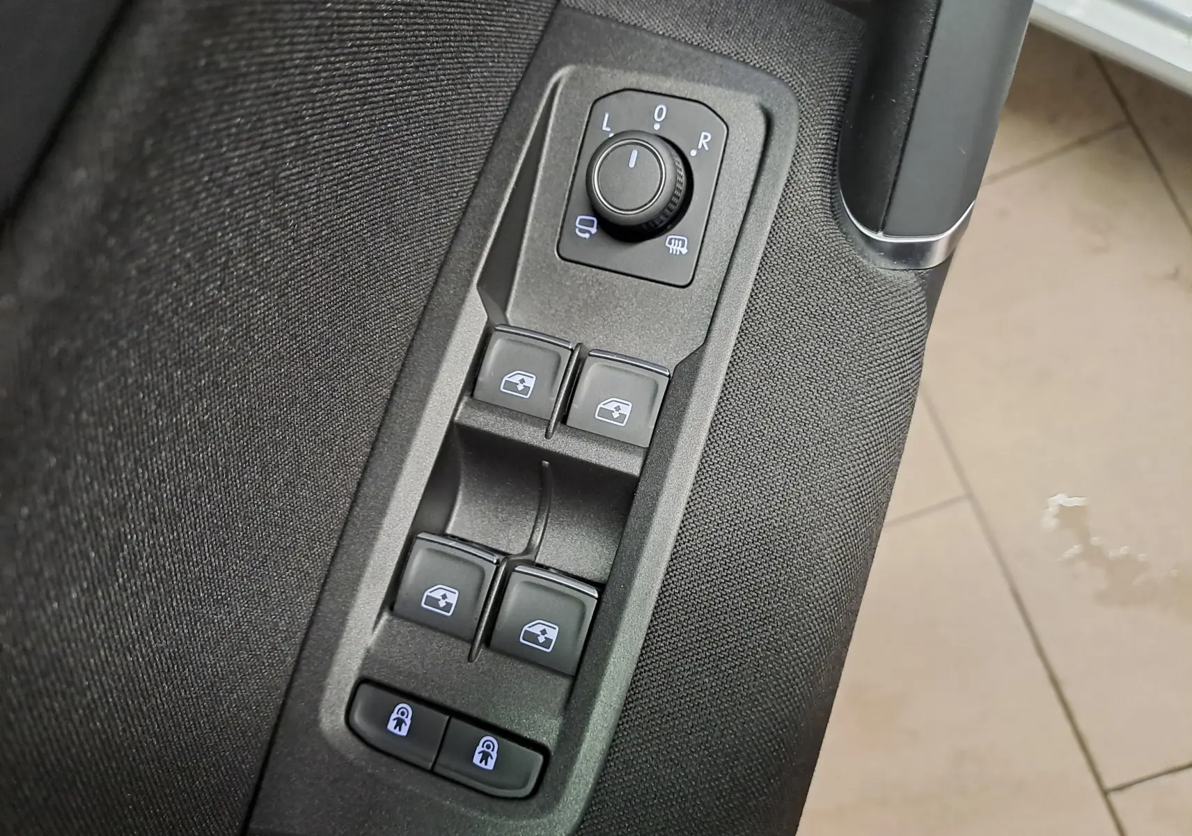 Gros plan sur les commandes de lève-vitres et réglage des rétroviseurs côté conducteur du Volkswagen Touran gris argent 2025.