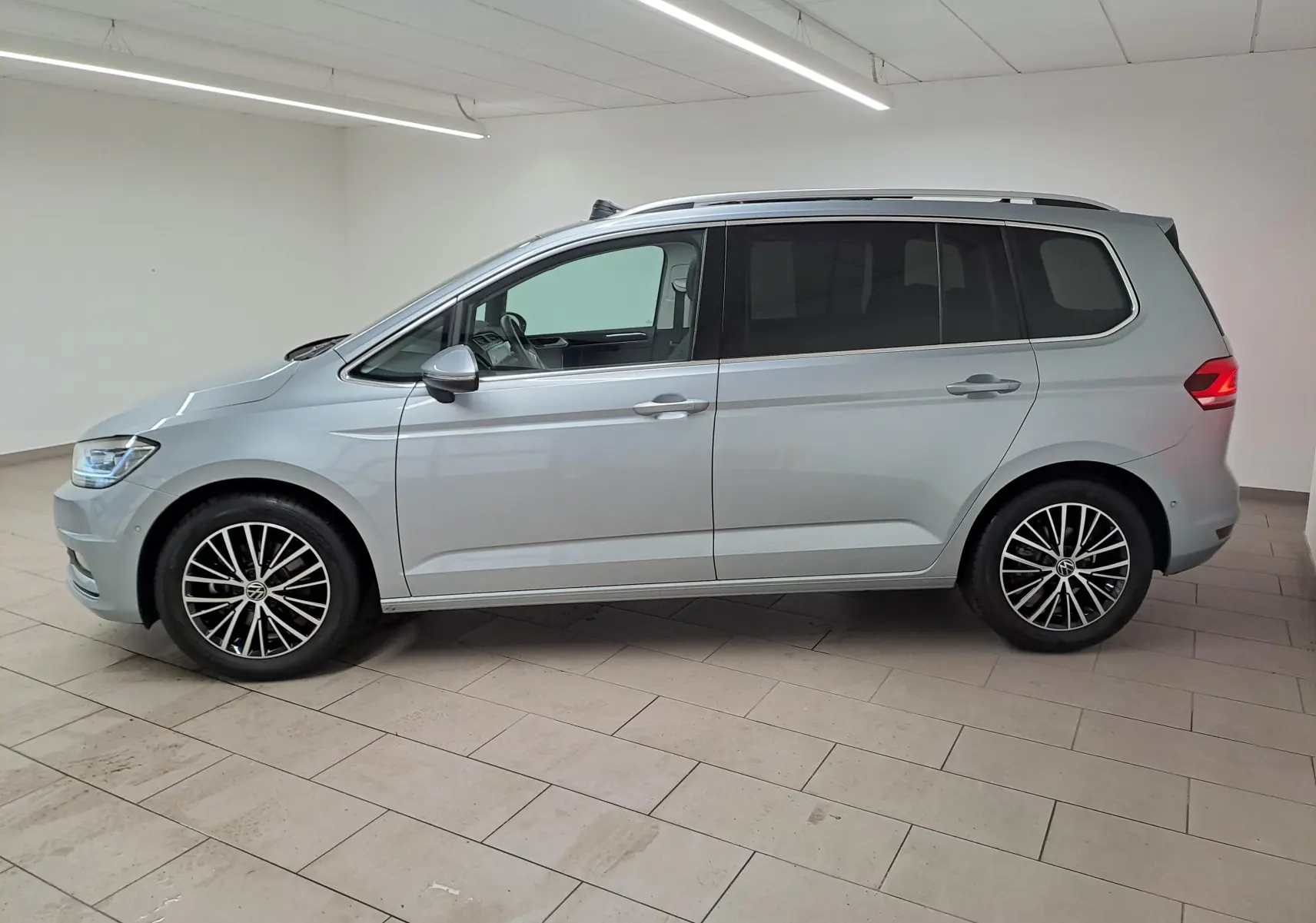 Vue 3/4 arrière droit d’un Volkswagen Touran gris argent avec hayon fermé et attelage escamotable visible en intérieur.
