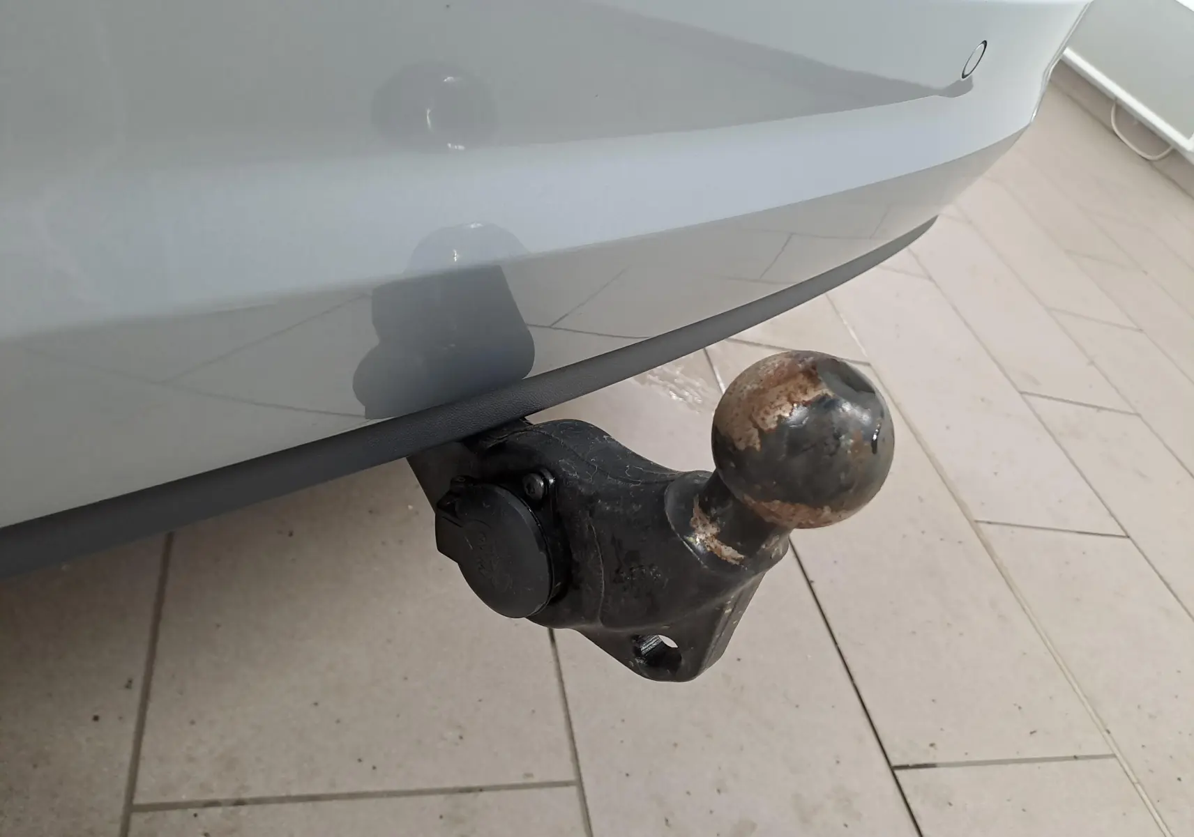 Gros plan sur le crochet d'attelage escamotable noir sous le pare-chocs arrière gris argent du Volkswagen Touran 2025.