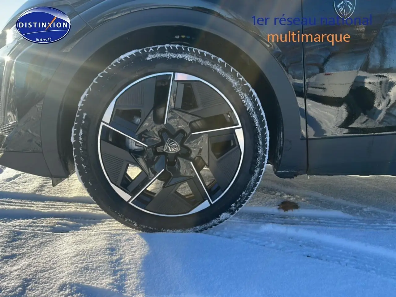 Gros plan sur la roue avant gauche d’une Peugeot 408 Hybrid 145 GT noire, avec jante alu et neige au sol.