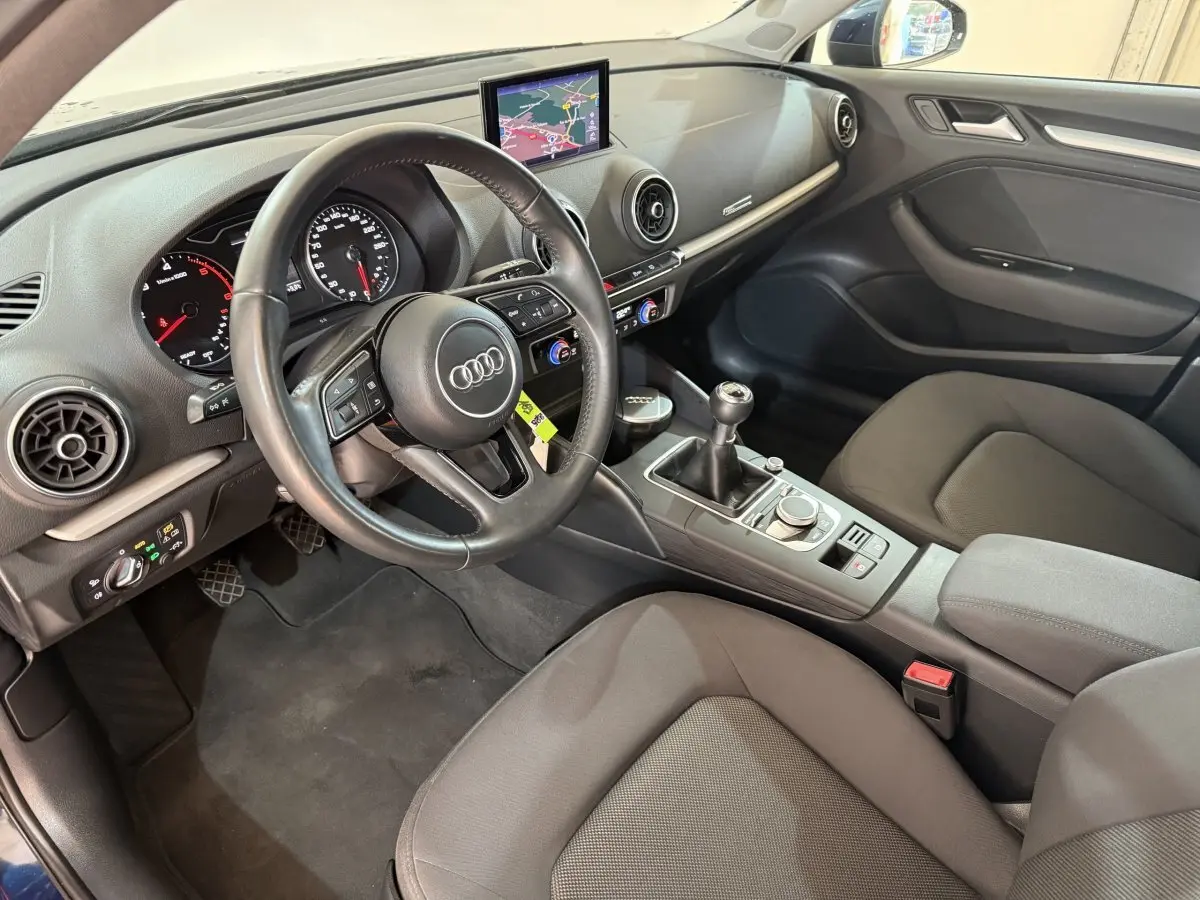 Vue intérieure côté conducteur de l'Audi A3 2.0 TDI 2018 avec volant cuir, écran navigation et levier de vitesse manuel.