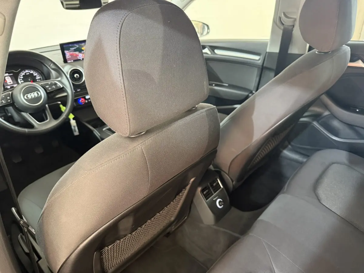Vue intérieure arrière de l'Audi A3 2018, sièges tissu gris et tableau de bord avec écran navigation visible.