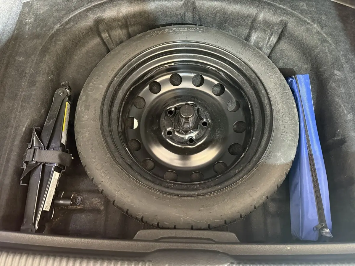 Gros plan sur la roue de secours galette noire dans le coffre de l'Audi A3 2.0 TDI bleu, avec cric et trousse à outils.