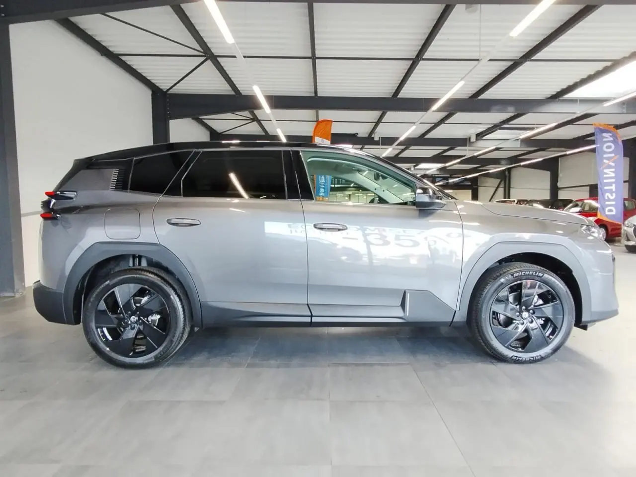 Vue de profil côté gauche d'un Citroën C5 Aircross gris platine avec jantes alliage noires en intérieur showroom.