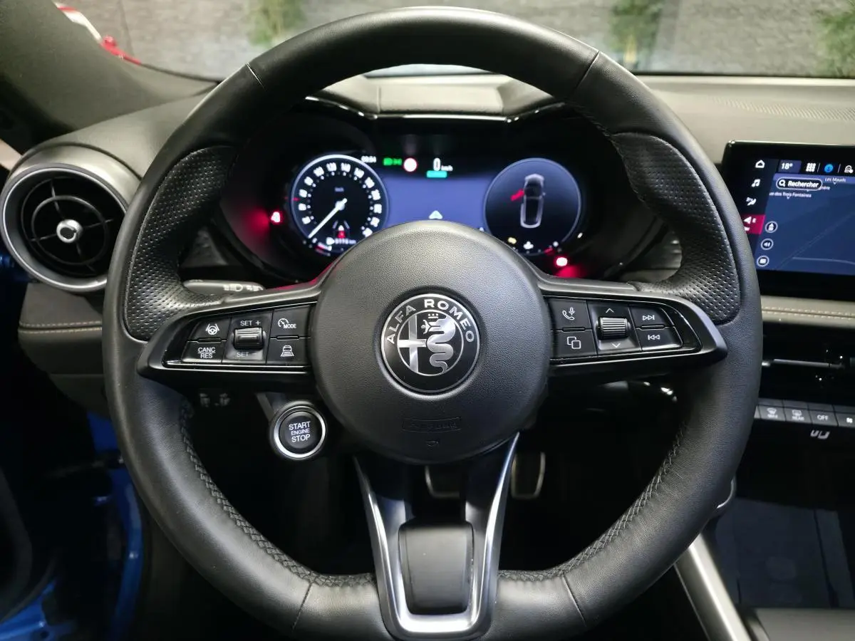 Vue rapprochée du volant cuir noir perforé de l'Alfa Romeo Tonale 2025 avec tableau de bord digital et bouton start/stop.
